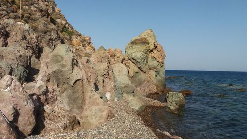 Rock formations by sea against clear sky