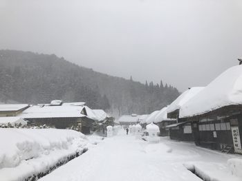 Snow covered houses by buildings against sky