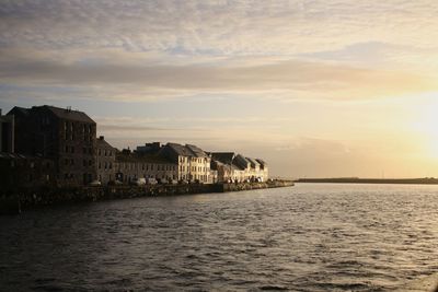 Buildings by sea against sky during sunset