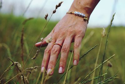 Cropped hand touching grass on field