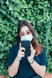 Portrait of young woman using phone while standing on plants