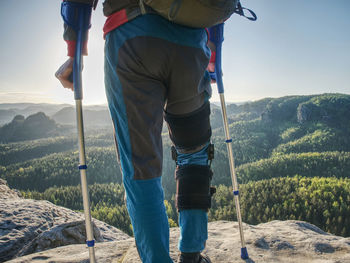 Injured tourist in detail with knee fixed in knee brace feature. scenic mountain top with valley