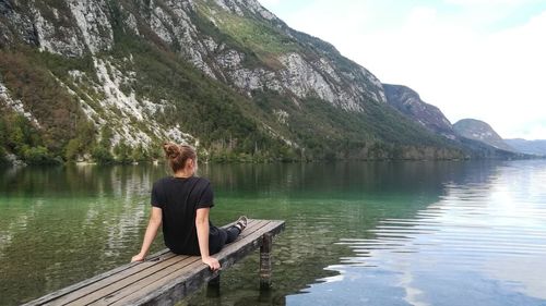 Woman standing on lake by mountain against sky