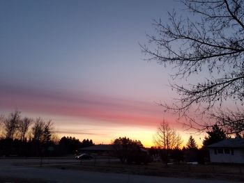 Bare trees against sky at sunset