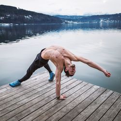 Full length of shirtless man standing on pier over lake