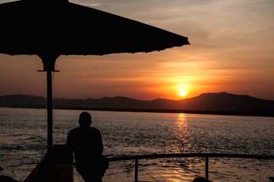 Silhouette man standing by sea against sky during sunset