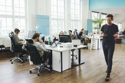 Businessman walking by colleagues working at desk in creative office
