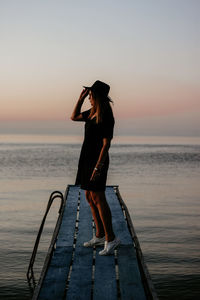 Woman standing at sea shore against sky during sunset