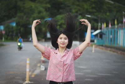 Portrait of young woman tossing hair while standing on road