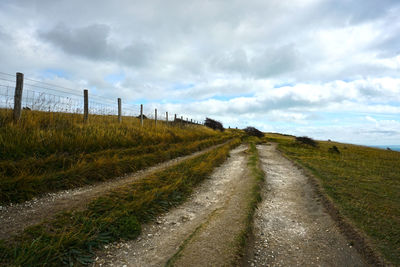 Empty road amidst field against sky