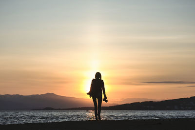 Silhouette man standing on sea against sky during sunset