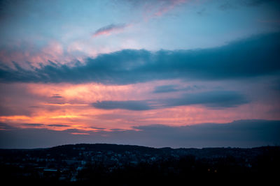 Silhouette city against dramatic sky during sunset