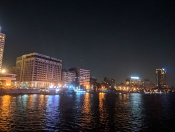 Illuminated buildings by sea against clear sky at night