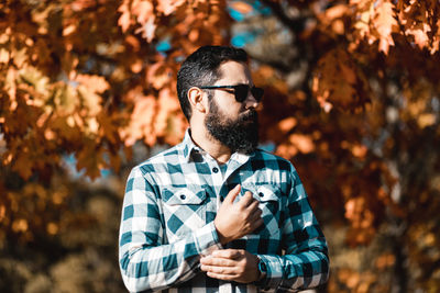 Man wearing sunglasses looking away while standing against trees