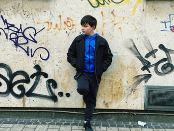 Full length of young man looking away while standing against graffiti wall