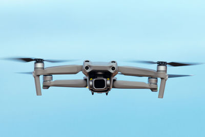 Contemporary unmanned aerial vehicle with camera and propellers flying against cloudless blue sky