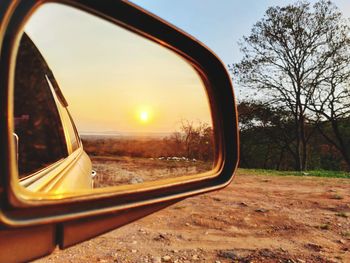 Reflection of trees and sky on side-view mirror during sunset