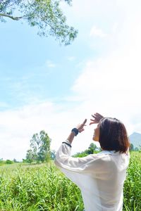 Rear view of woman holding umbrella on field against sky