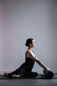 Side view of young woman sitting on floor against wall