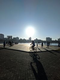People riding bicycle on street in city against bright sun