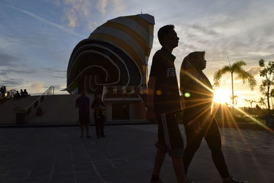 People walking in city against sky during sunset