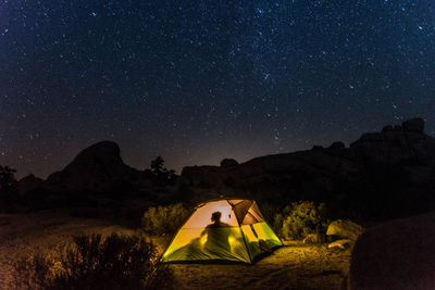 Shadow of person sitting in tent by sky with stars at night