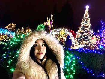 Portrait of woman with illuminated christmas tree at night