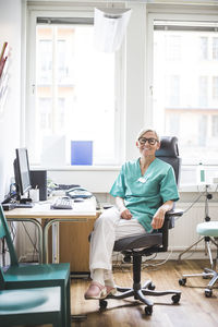 Full length portrait of smiling mature female doctor sitting in clinic