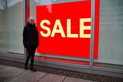 Full length of woman standing against sale sign