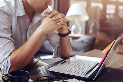 Midsection of man using laptop on table at home