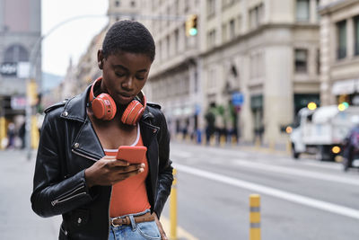 Young woman with headphones using smart phone while standing in city