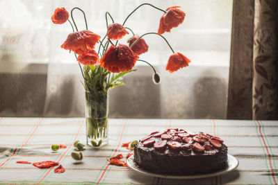 Poppies in vase by cake on table at home