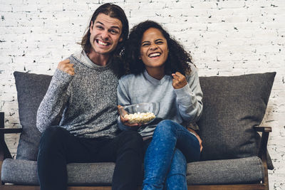 Portrait of smiling couple gesturing while sitting with popcorn on sofa