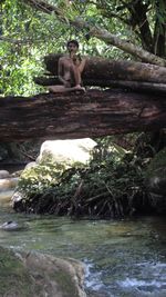 Young woman sitting by river in forest