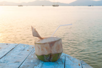 Close-up of coconut on table against sea during sunset