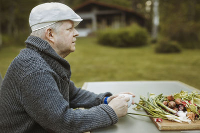 Side view of mature man sitting at table with freshly harvested vegetables