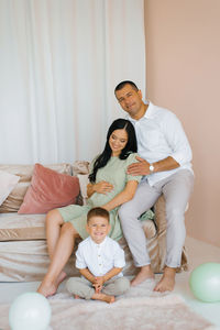 Pregnant woman is sitting on a sofa surrounded by her husband and son person