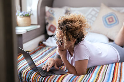 Side view of woman sitting on bed at home