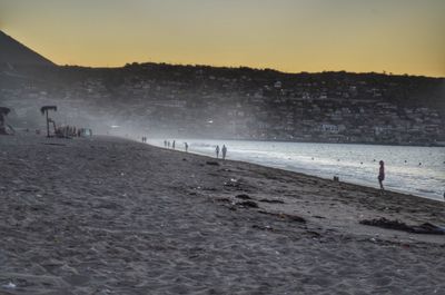 People at beach against sky during sunset