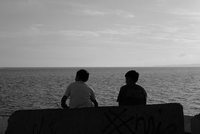 Rear view of men looking at sea against sky