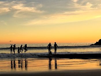 Silhouette of children jumping waves at beach against sky during sunset with reflections 