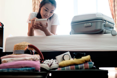 Woman writing on book with luggage at home