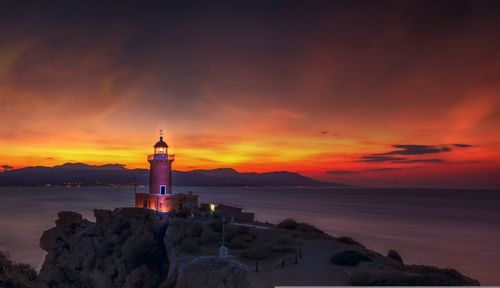 Lighthouse by sea against sky during sunset