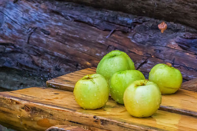 Close-up of wet green apples on wooden bench during rainy season