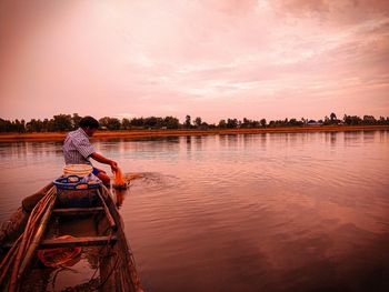 Rear view of man sitting on boat in lake against sky