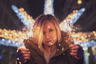 Portrait of woman holding illuminated sparkler at night