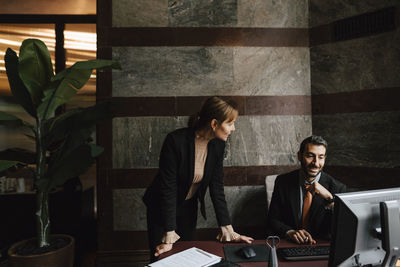 Businesswoman leaning on desk discussing with businessman at law office