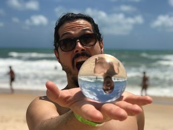 Portrait of mature man holding sunglasses at beach