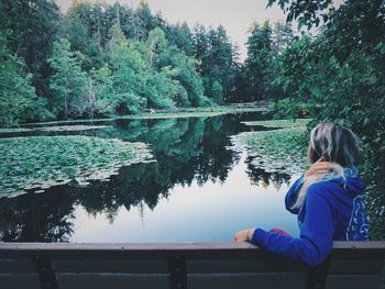 Woman sitting at lakeshore against trees