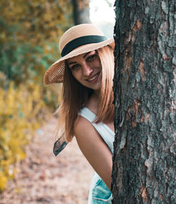 Young woman wearing hat standing by tree trunk
